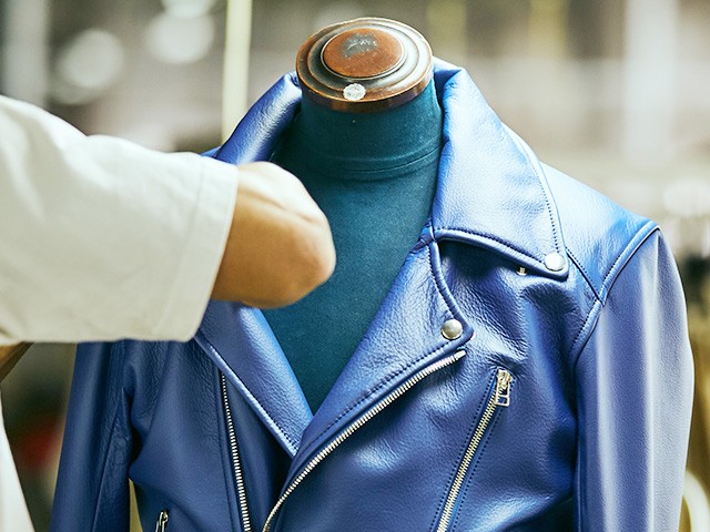 トルソーに着せたブルーのライダースジャケットを職人が仕上げている様子